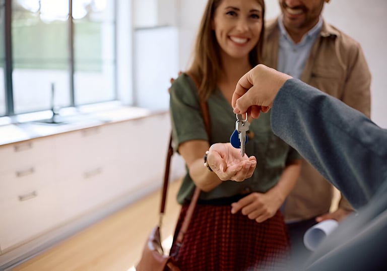 Mujer recibiendo llave de su nueva vivienda en compañía de su pareja, reflejando entrega de proyecto