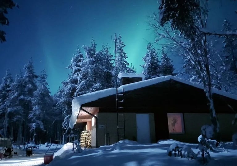 Chalet enneigé en Laponie avec des aurores boréales illuminant, le ciel nocturne et des arbres