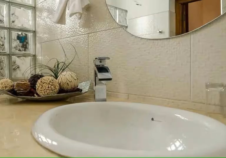 Modern bathroom vanity featuring a white drop-in sink, chrome faucet, and glass block wall.
