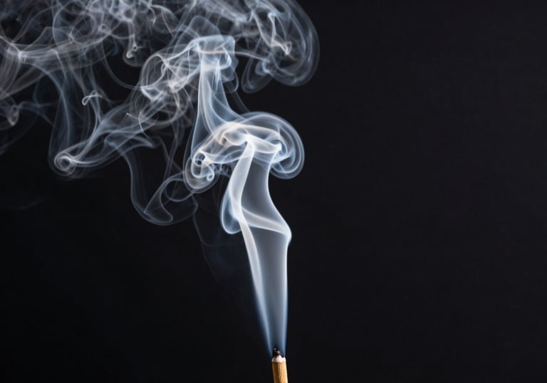 A column of thick mist white incense smoke rising vertically against a solid charcoal black background.