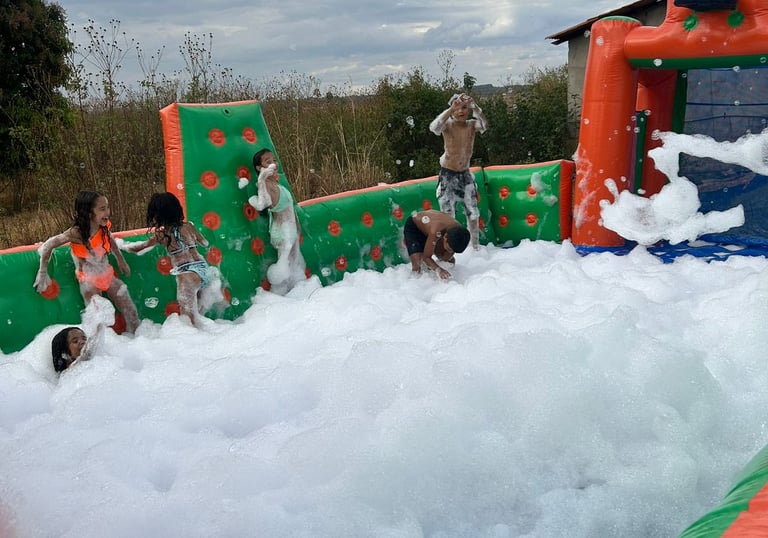 Excited children playing in a large inflatable foam pit at an outdoor summer party.