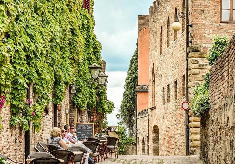 People enjoying coffee at an outdoor terrace on a charming historic street in Certaldo Alto, Tuscany