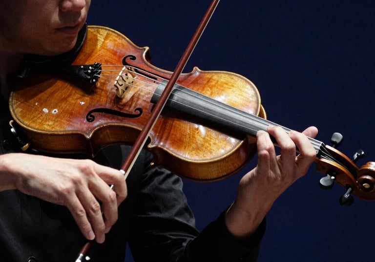 Close-up photography of a violinist's hands and bow during a performance. Dramatic lighting against a dark navy blue background highlights the rich wood tones.