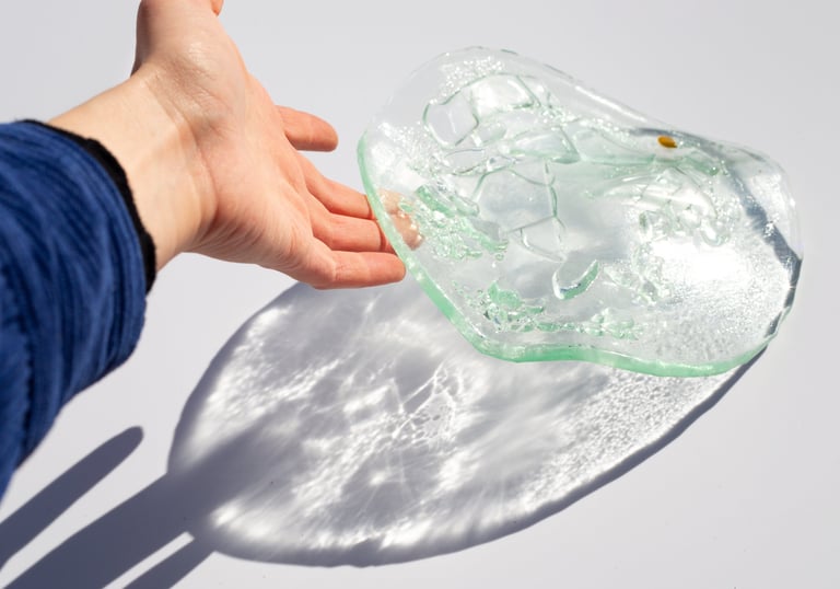 Una mano extendiéndose hacia un cuenco texturizado de vidrio, proyectando reflejos de luz brillante