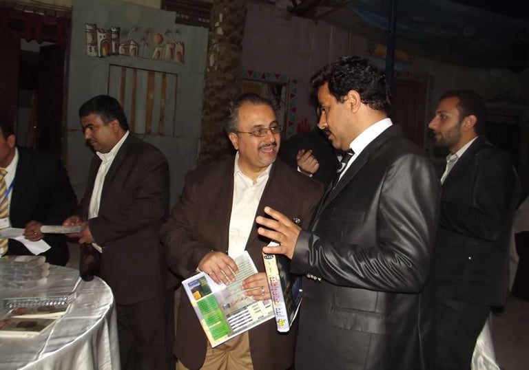 Professional men in suits networking and holding brochures at a formal evening event.