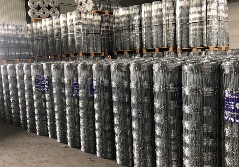 Stacks of galvanized cattle fence wire rolls neatly arranged in a warehouse, showing the bulk storage of livestock fencing pr