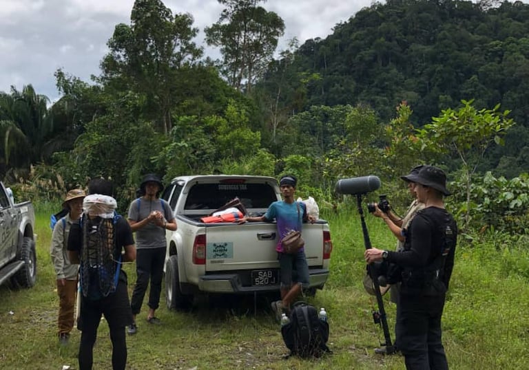 Jungle documentary filming team with local guides preparing equipment in Borneo rainforest Malaysia