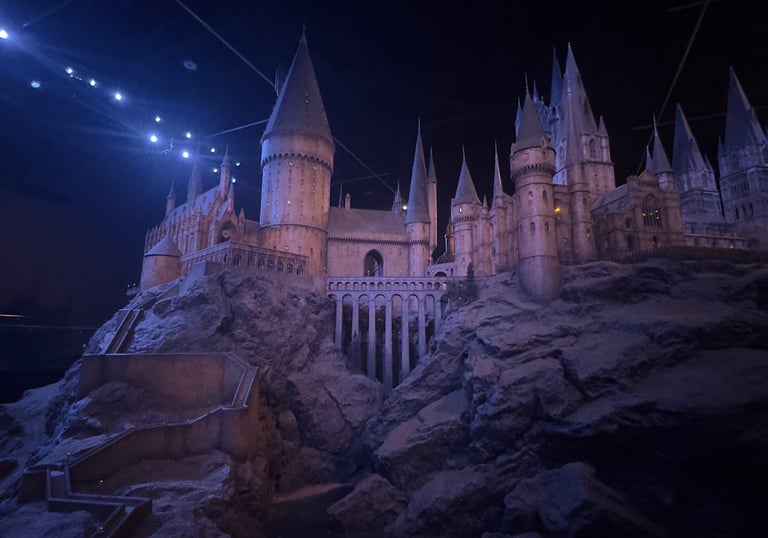 Detailed scale model of Hogwarts Castle with stone towers and bridges under dramatic blue lighting.