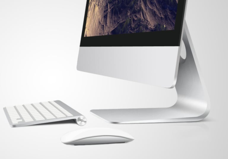 Un élégant ordinateur de bureau argenté avec clavier et souris sans fil, posé sur un bureau blanc