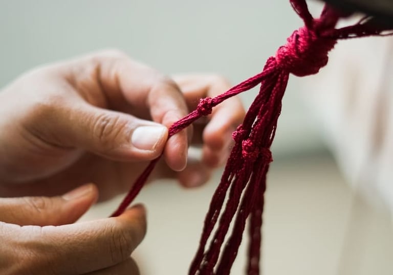 Hands tying a decorative red string knot for traditional handmade craft design.