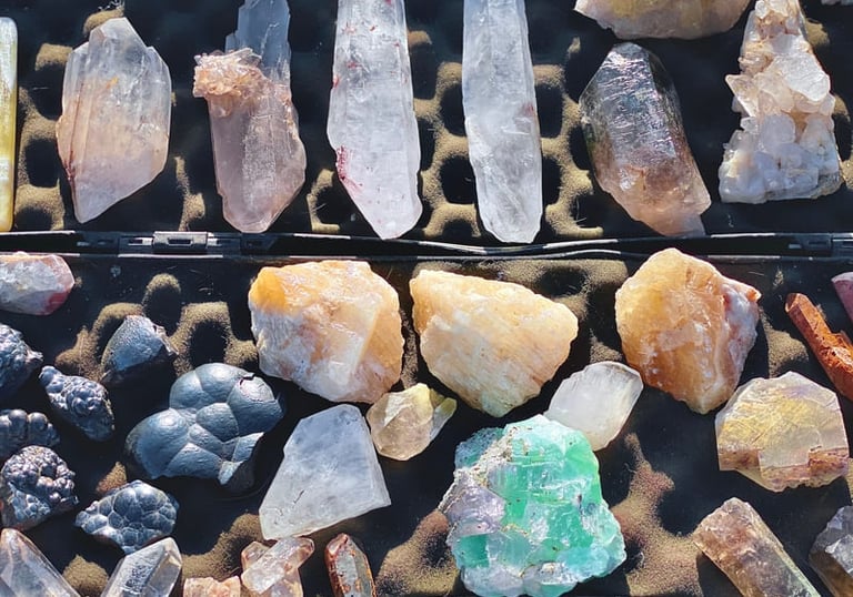A collection of raw healing crystals including clear quartz points, citrine, and green fluorite displayed in a case.