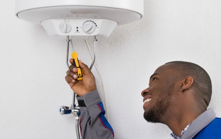 Professional plumber repairing an electric water heater unit with a handheld tool.