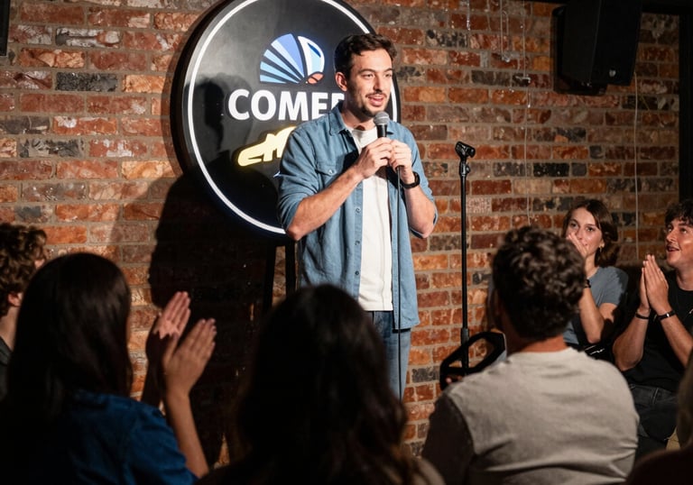 Stand-up comedian performing a live comedy set on stage for a laughing audience in a brick-walled club.