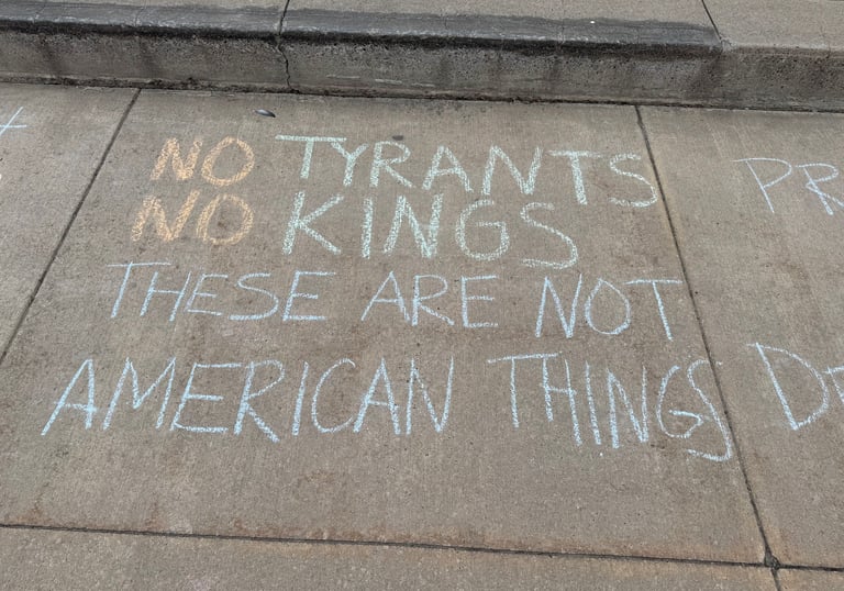 Sidewalk chalk art protest message reading No Tyrants No Kings These Are Not American Things.