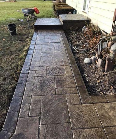 Custom dark brown stamped concrete walkway with a textured slate pattern leading to a home entrance.