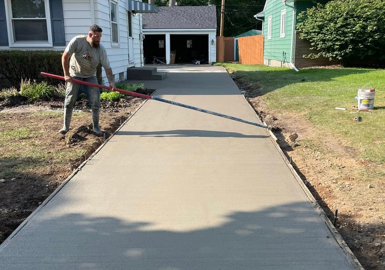 Professional contractor finishing a fresh concrete driveway installation with broom finish.