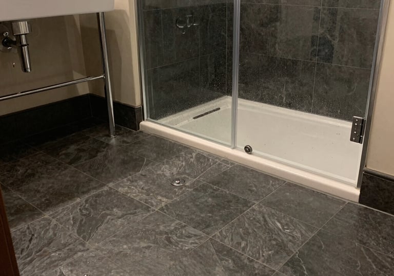 Spotless bathroom featuring a clean glass shower enclosure and scrubbed dark tile floors after a dee