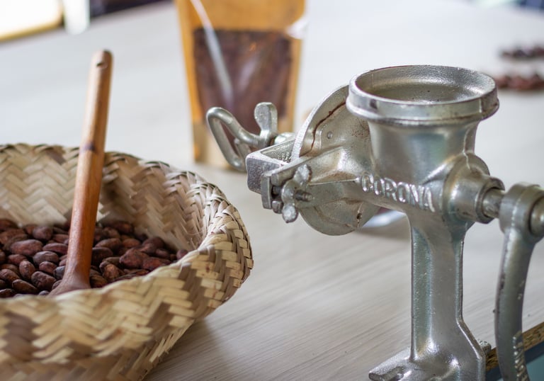 Vintage metal manual grinder next to a woven basket of raw cocoa beans for chocolate making.