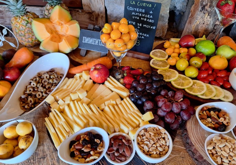 Gourmet charcuterie board with sliced Gruyere and Emmental cheese, fresh grapes, nuts, and tropical fruits.