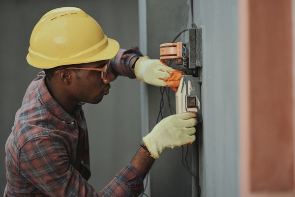 Professional electrician in a yellow hard hat installing a residential electrical panel.