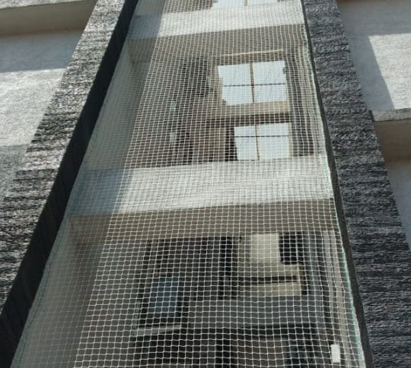 Installation team fitting pigeon nets around an AC unit in a residential building.