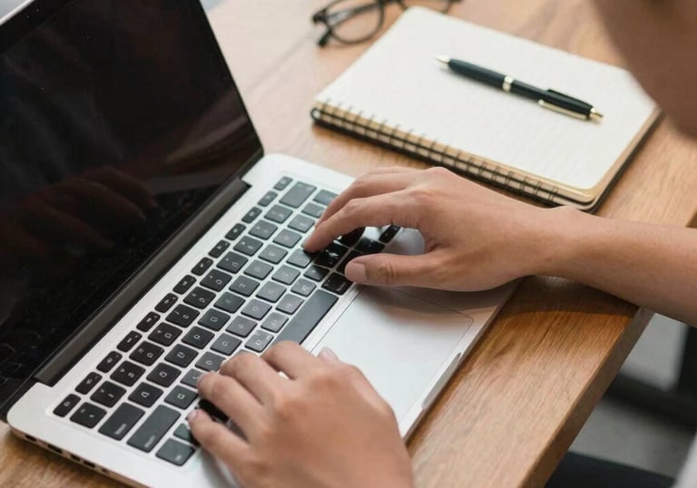 A top-down view of a person using a laptop and a notebook in a modern cafe in Indonesia, focus on hands and technology, clean and warm atmosphere.