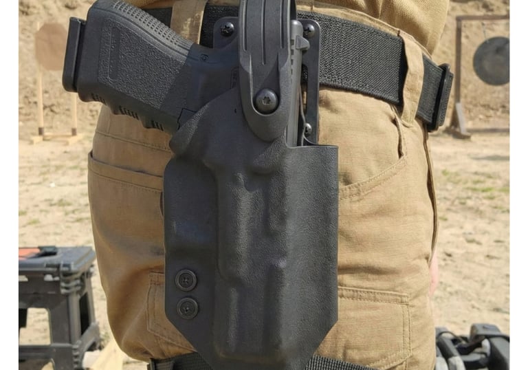 Close-up of a black tactical kydex holster with a handgun secured on a shooter's hip at an outdoor range.