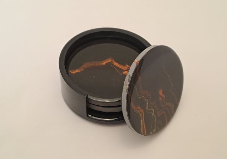 Handcrafted dark coasters in a holder, with black and amber marbled coaster propped up to show its p