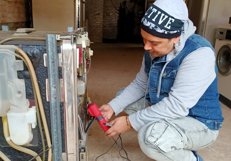 Professional technician using a digital multimeter to repair a disassembled dishwasher in a workshop.
