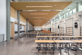 Modern school cafeteria interior with wooden ceiling panels and folding lunch tables.