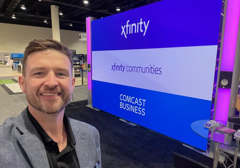 Chris takes a selfie in front of a blue Xfinity Comcast Business booth at a professional trade show.
