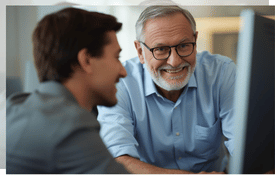 a man sitting at a computer desk with a man in a blue shirt