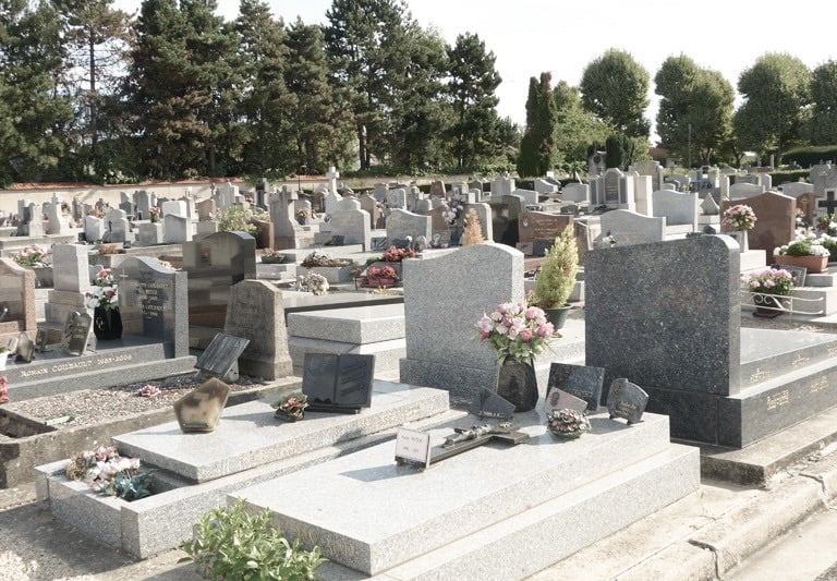 Granite tombstones and memorial monuments with fresh flowers in a peaceful cemetery landscape.