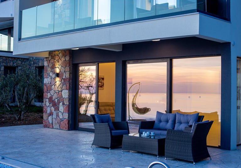 Stunning Mediterranean terrace at sunset with modern glass doors, comfortable seating and stone acce