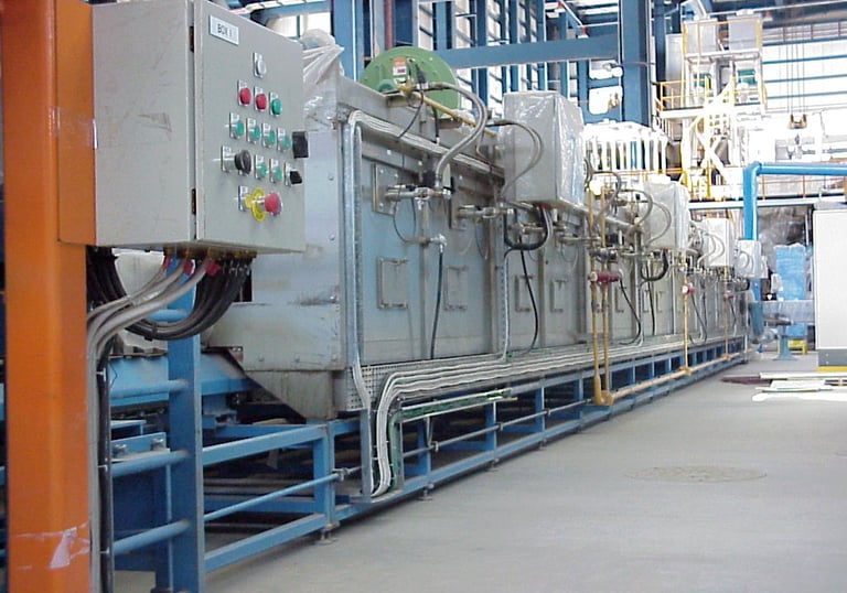 Conveyor oven machine with control panels in a manufacturing factory setting.
