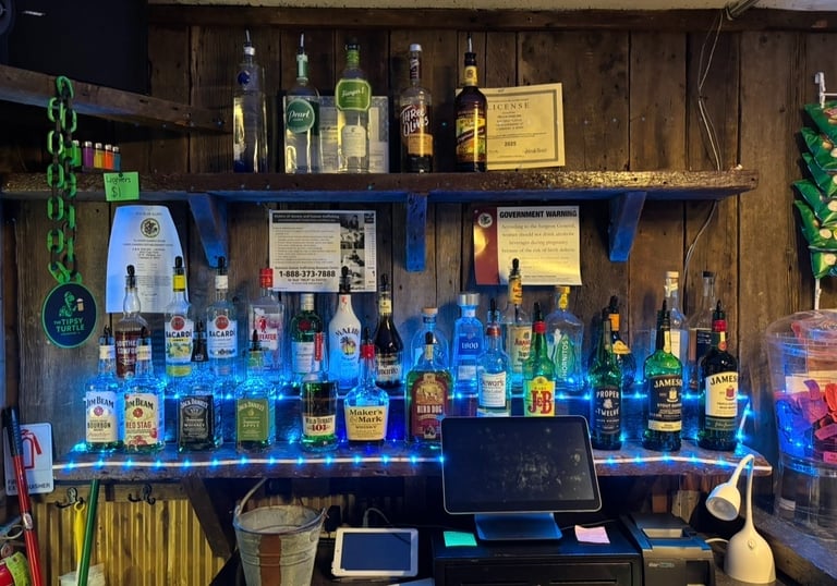 Rustic wood bar back shelf displaying various liquor bottles illuminated by blue LED lights.