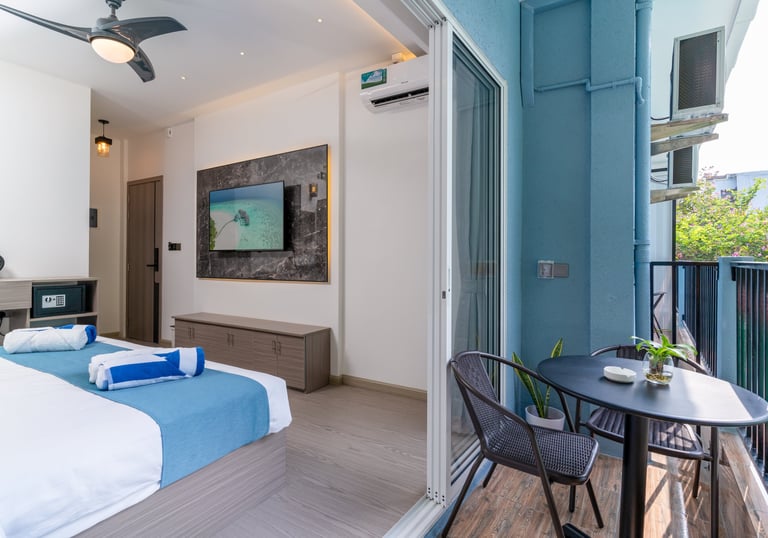 Modern hotel room with blue accents, flat-screen TV, and a private balcony with outdoor seating.