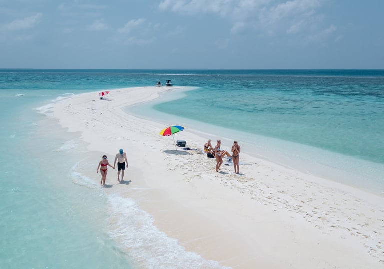 Aerial view of tourists relaxing on a white sandbar surrounded by turquoise ocean water in the Maldives.