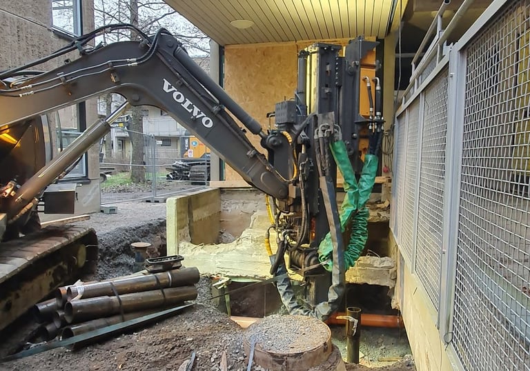 A Volvo excavator performs foundation drilling and piling at a modern urban construction site.