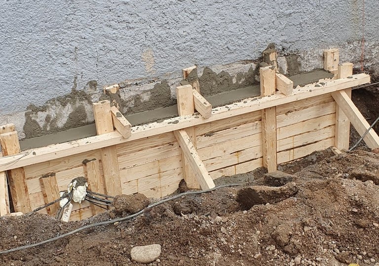 Wooden formwork for a new concrete foundation wall being poured against an existing building.