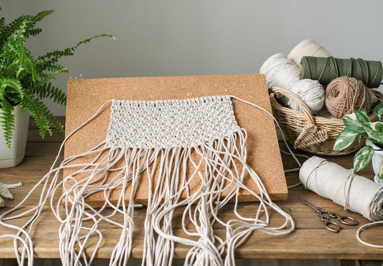 Proyecto de tapiz de macramé hecho a mano fijado con alfileres a un tablero de corcho.