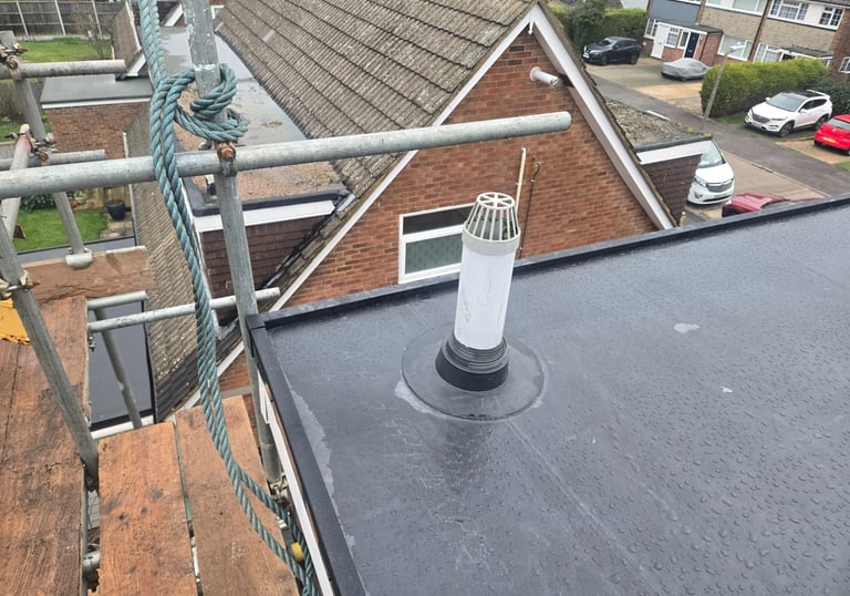 Flat roof installation with a white vent pipe and waterproof seal surrounded by scaffolding.