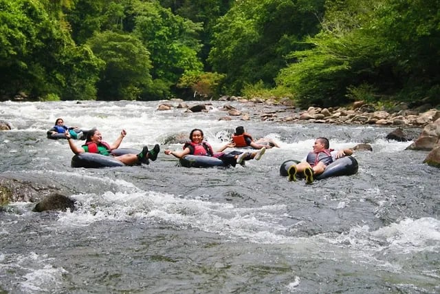 Group of tourists enjoying river tubing through white water rapids in a tropical jungle.