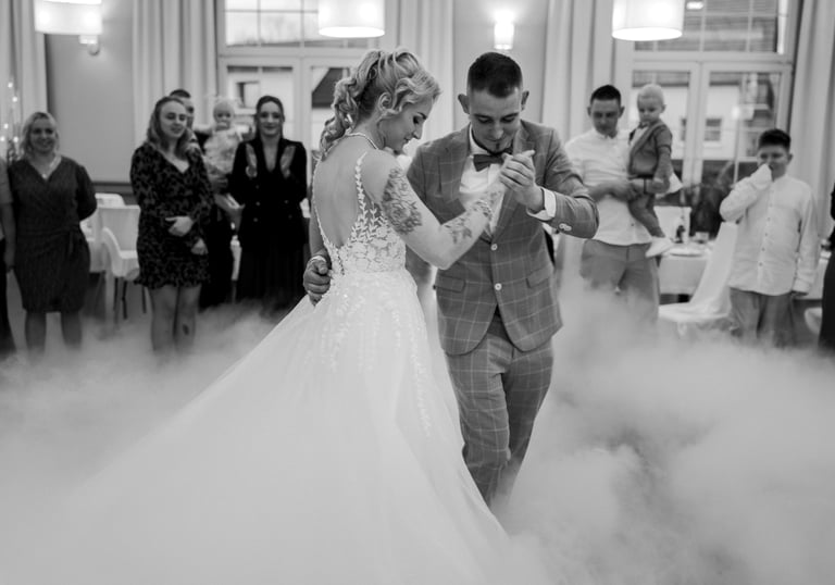Black and white photo of a bride and groom dancing on a floor covered in low fog during their wedding reception.