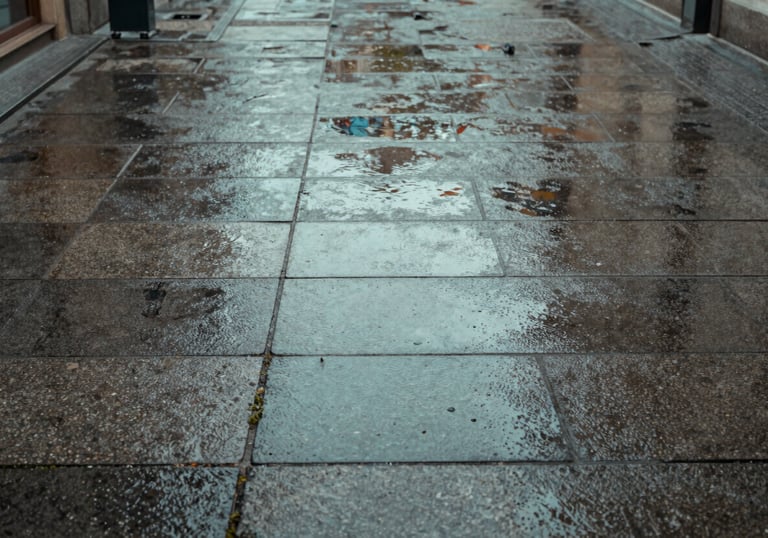A close-up of clean, power-washed stone pavement in a Central European / German commercial courtyard. The stones are wet, reflecting the Muted Teal sky. No weeds, perfectly maintained.