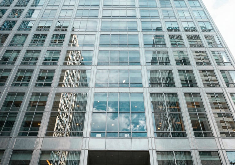 An architectural shot of a glass-and-steel skyscraper lobby in the United States. The perspective is looking up, conveying authority with light blue and white tones.