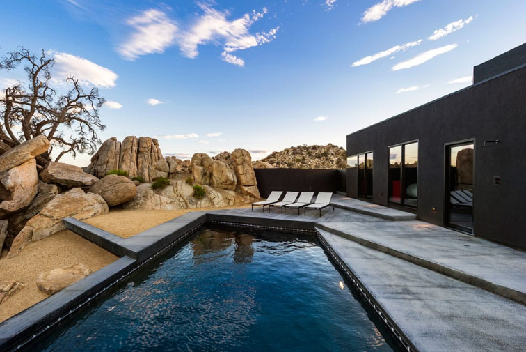 Angular desert-style pool with dark charcoal water and matching dark tiling for a modern, rugged loo