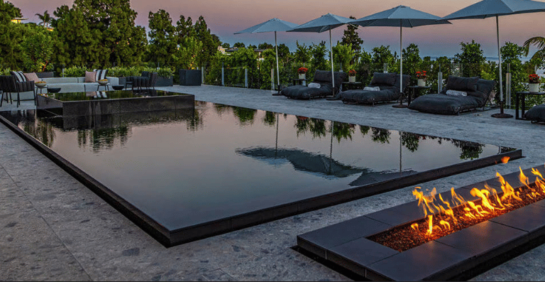 Reflective geometric pool with dark mirror-like water and charcoal tiling beside a modern fire featu