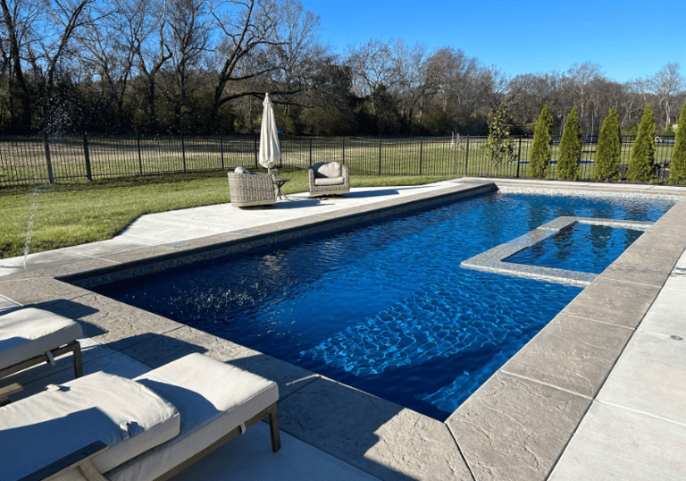 Rectangular pool with deep blue water and light stone tiling, featuring a built-in tanning ledge.