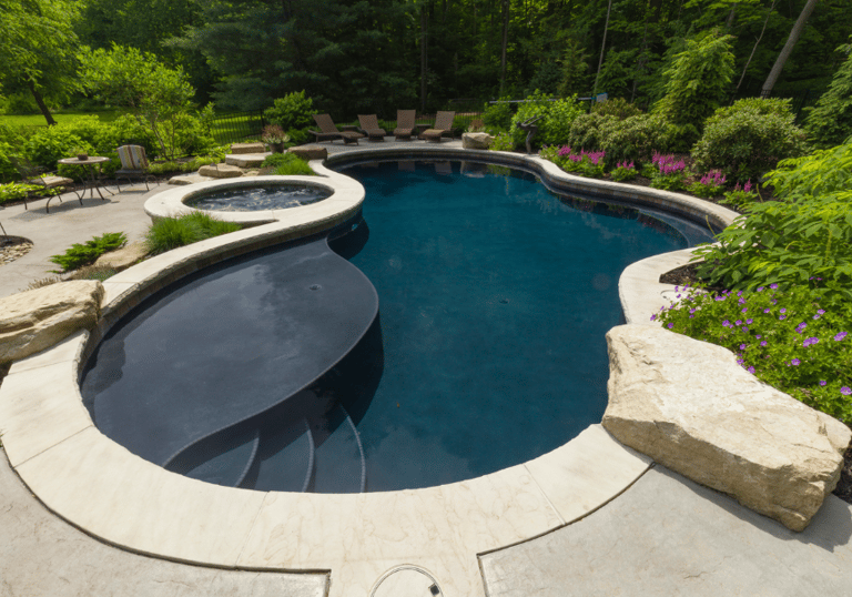 Freeform lagoon pool with dark teal water and light stone coping, paired with a curved built-in spa